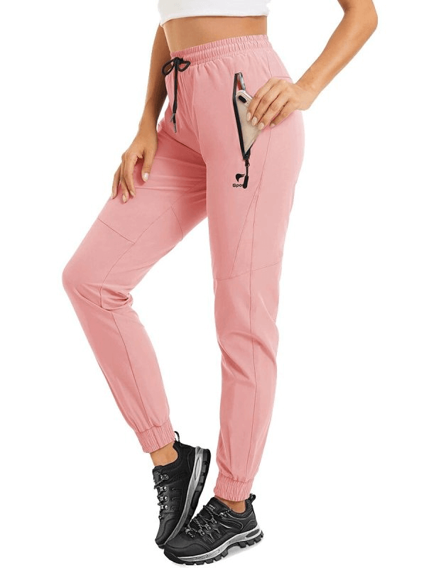 Woman wearing pink quick-drying travel pants with zippered pockets, drawstring waist, and sneakers ideal for active outdoor activities.